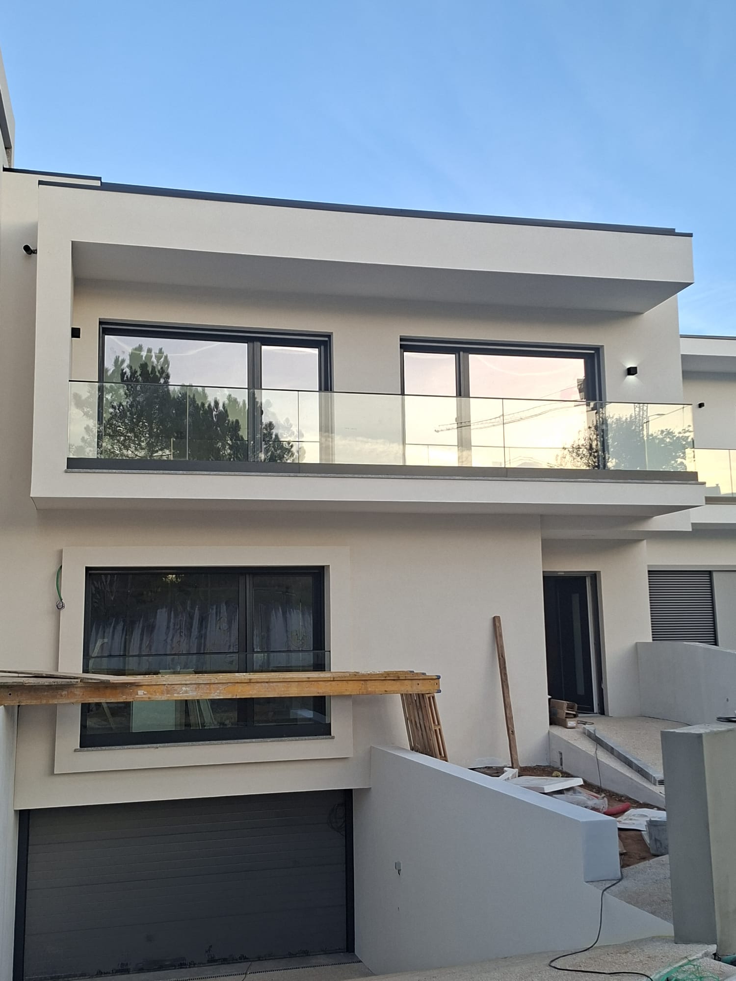 Vista frontal de uma varanda com guarda-corpos em vidro numa moradia em obra